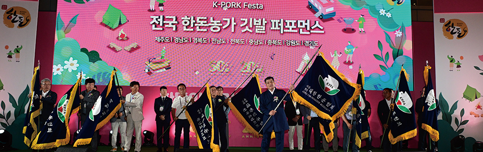 전국 한돈농가 깃발 퍼포먼스 글자가 떠있는 전광판 앞에 일렬로 많은 사람들이 서있는 모습